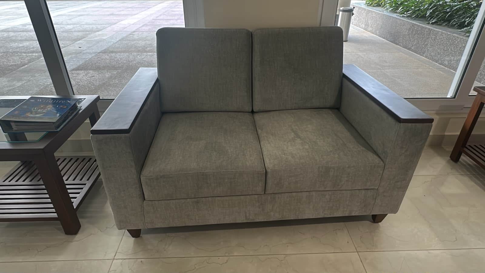 A modern two-seater loveseat with a light grey fabric upholstery and dark wood panels integrated int… — 3D model