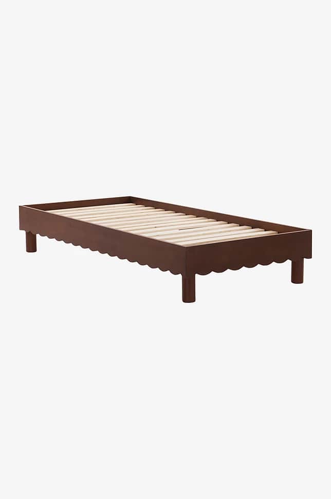A bed frame with a scalloped edge along the side rails and four cylindrical legs. The frame supports… — 3D model