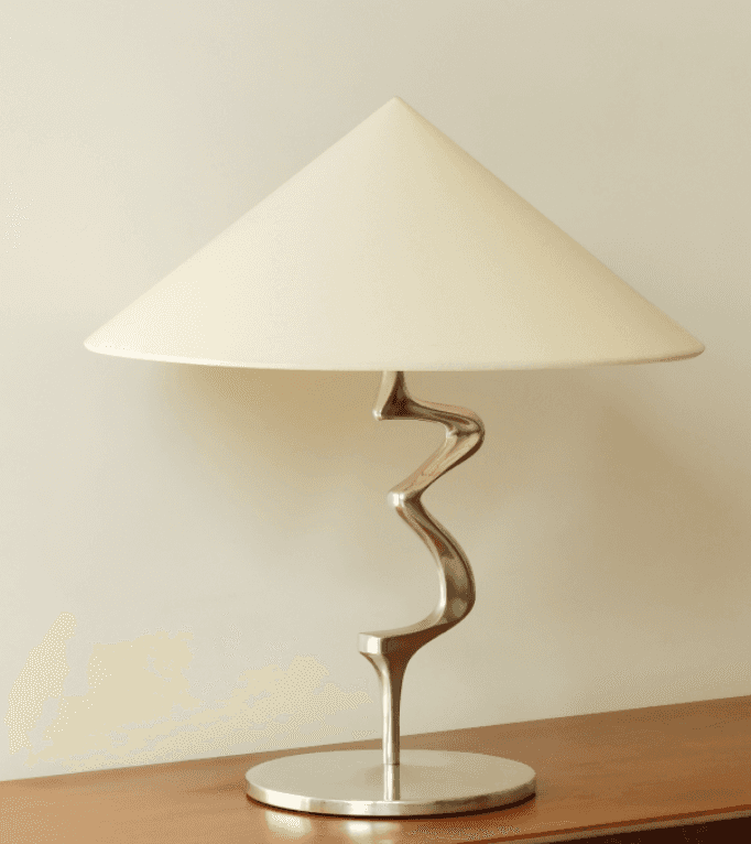 A modern table lamp featuring a distinctive serpentine metal stem, a circular base, and a conical fa… — 3D model