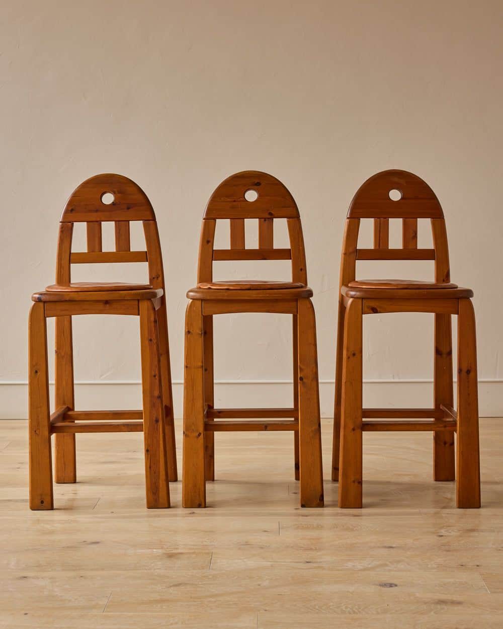 A wooden bar stool featuring a natural finish, a slatted backrest with an arched top rail, a circula… — 3D model
