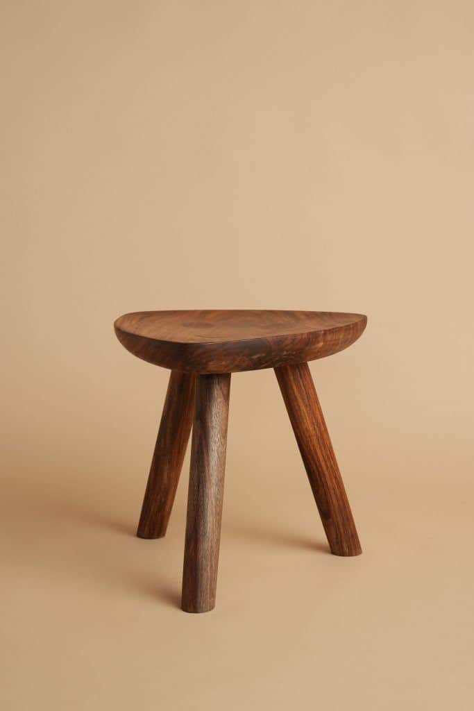 A sculptural three-legged stool crafted from solid dark wood, featuring a concave, saddle-shaped sea… — 3D model