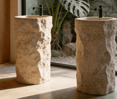 A tall, freestanding pedestal sink made from light-colored, rough-hewn natural stone, featuring an i… — 3D model