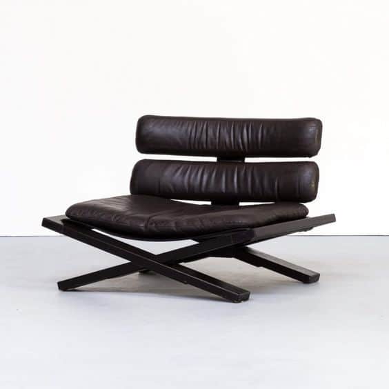 A modern low-profile lounge chair featuring a distinctive black X-frame base and rich brown leather… — 3D model