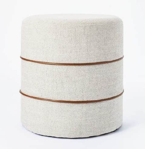 A contemporary cylindrical ottoman featuring off-white textured fabric upholstery and two thin, dark… — 3D model