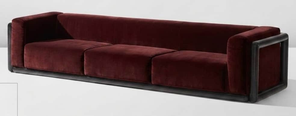 A long, three-seater sofa upholstered in deep burgundy velvet, featuring a minimalist dark wooden or… — 3D model