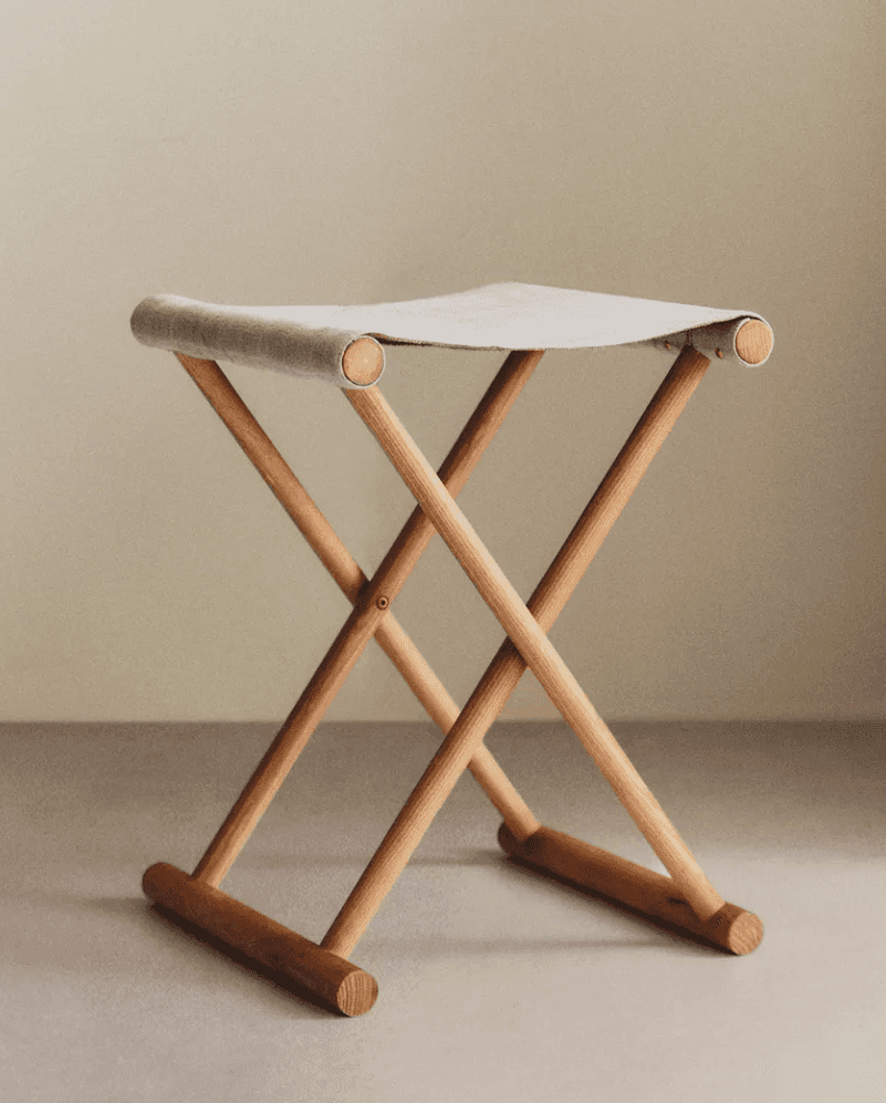 A lightweight, portable folding stool featuring an X-frame design crafted from light-toned wood. The… — 3D model