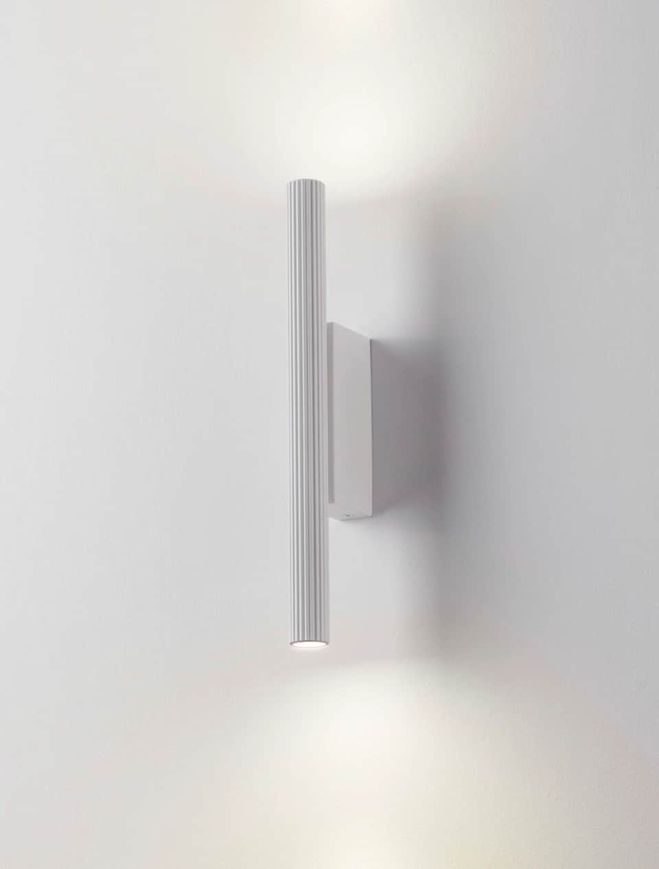 A contemporary white wall sconce featuring a vertical, cylindrical body with a distinctive ribbed te… — 3D model
