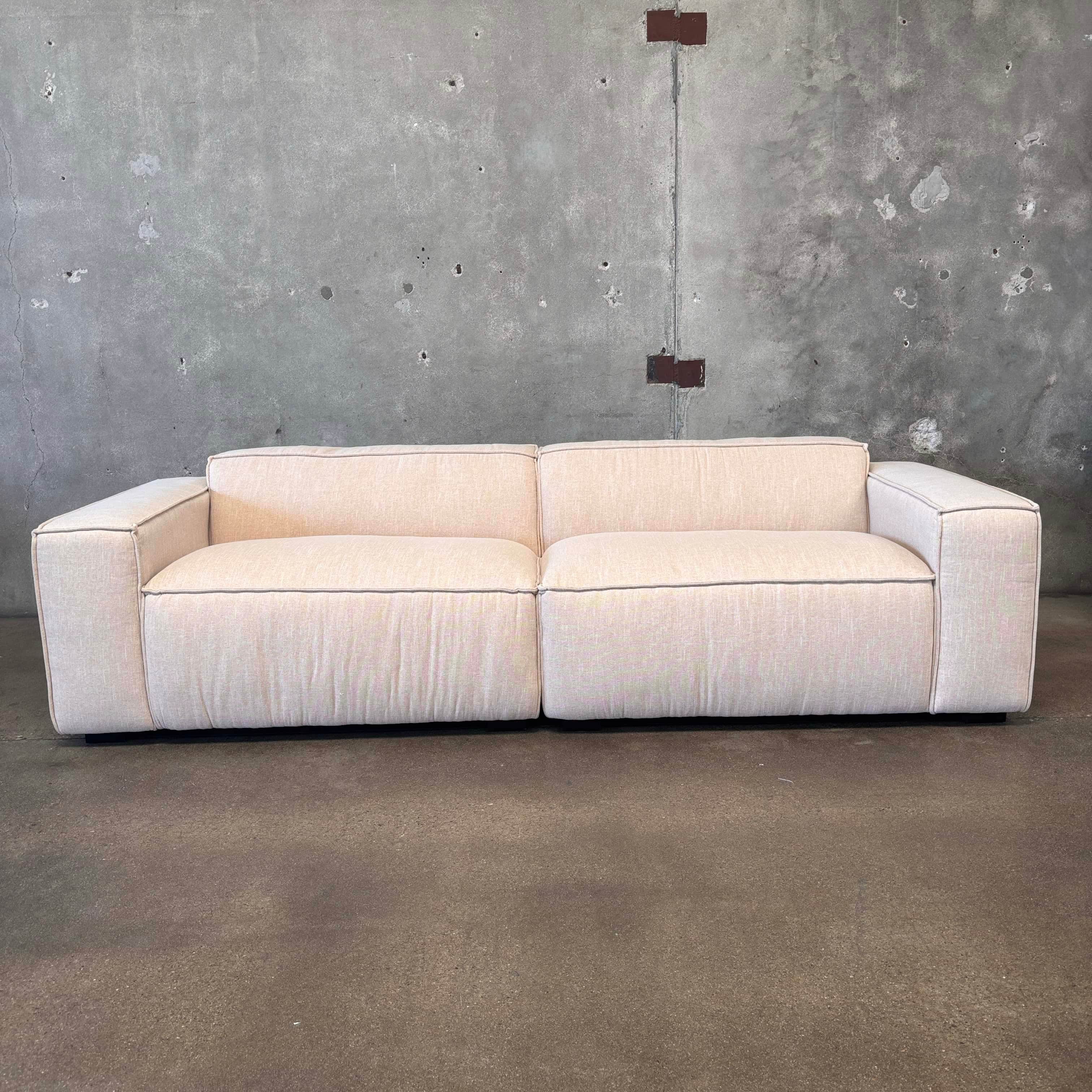 A modern, two-seater sofa with a low profile and blocky arms. The sofa is upholstered in a light-col… — 3D model