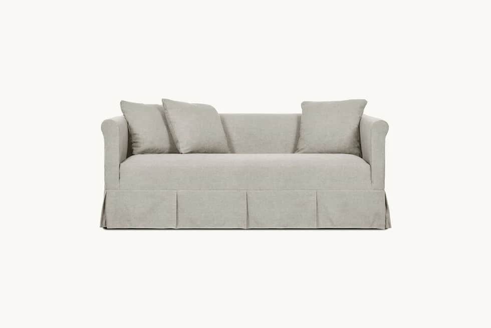 A light-colored, slipcovered sofa with a tailored skirt featuring pleats. It has plush seat and back… — 3D model