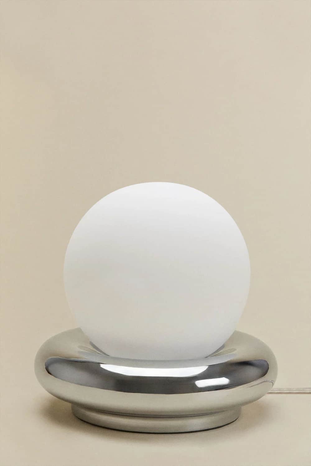A modern table lamp featuring a spherical frosted white glass diffuser resting within a polished chr… — 3D model