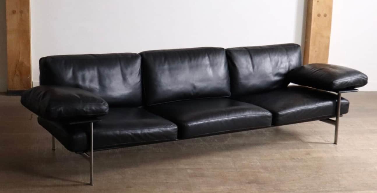 A modern three-seater sofa upholstered in black leather, featuring a minimalist design with a visibl… — 3D model