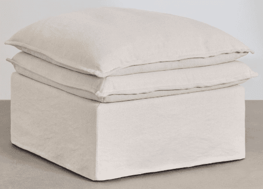 A light beige, square, slipcovered ottoman featuring a boxy base and two stacked, plush cushions on… — 3D model
