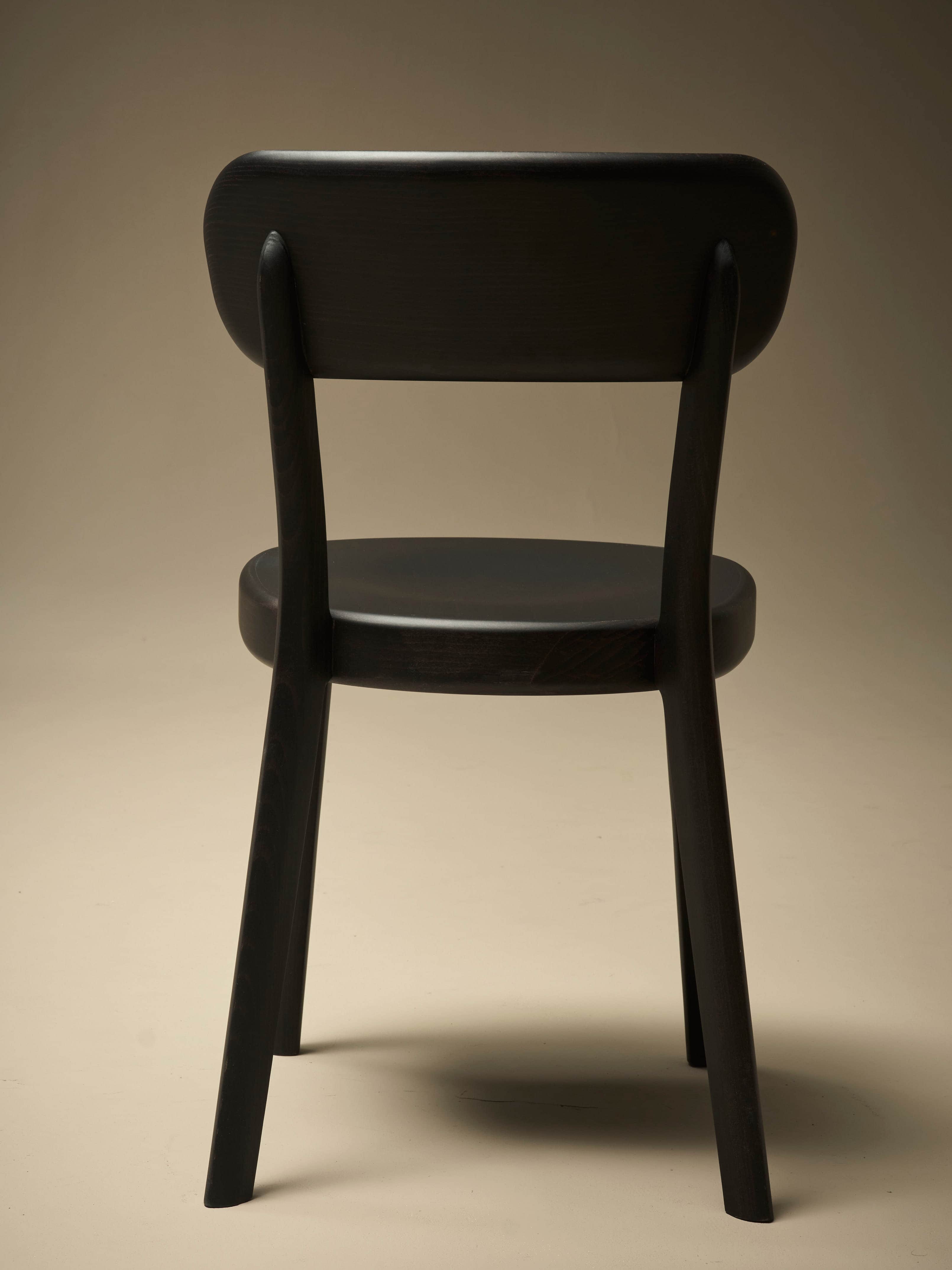 A dark-colored wooden dining chair viewed from the back. The chair features a gently curved backrest… — 3D model