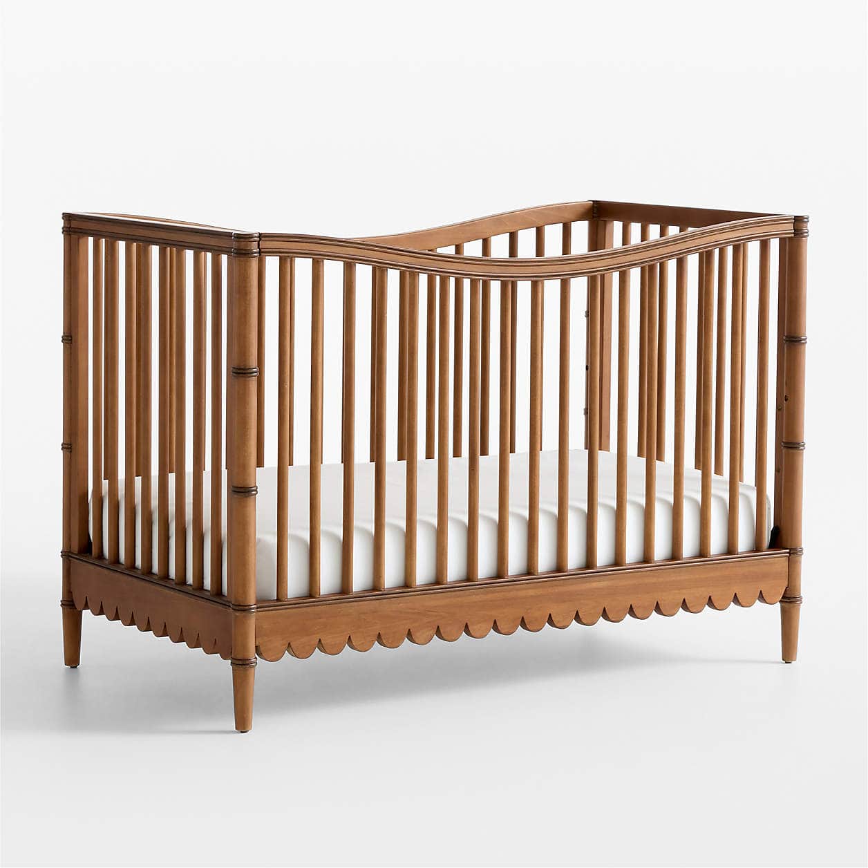 A wooden crib with a scalloped bottom edge and turned legs. The crib features vertical spindles and… — 3D model