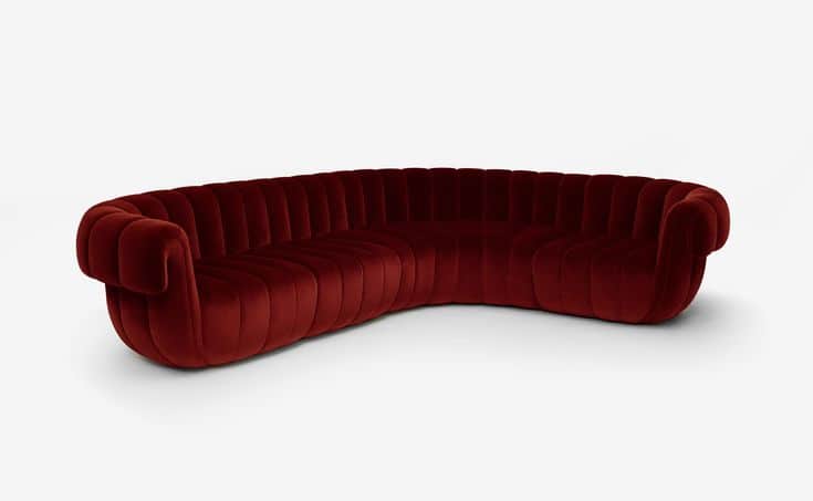 A large, elegantly curved sofa upholstered in deep red velvet, featuring prominent vertical channel… — 3D model