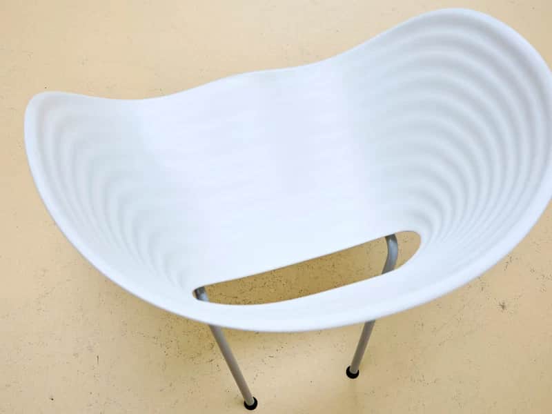 A modern white molded chair featuring a distinct wavy, ridged surface texture and a unique cutout in… — 3D model