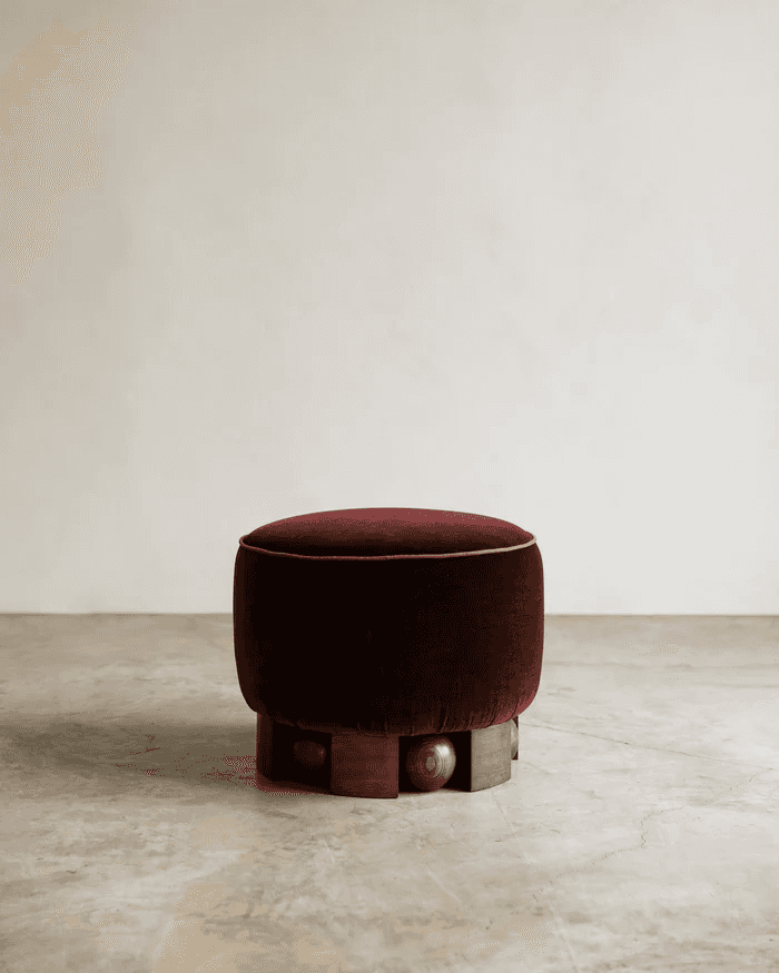 A round, upholstered ottoman with a deep red velvet fabric. The ottoman is characterized by a decora… — 3D model