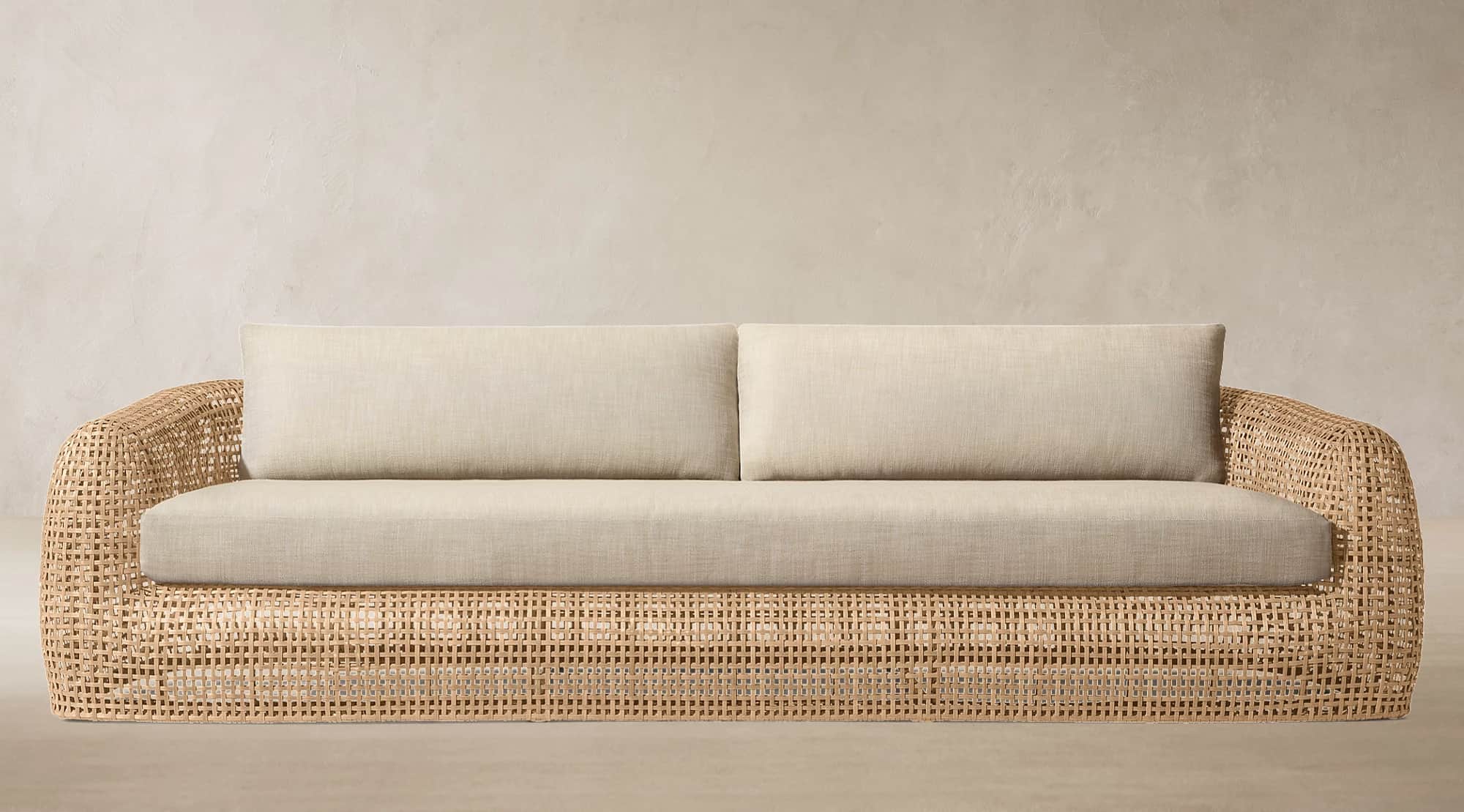 A contemporary sofa featuring a curved, open-weave rattan frame and soft, light-colored upholstered… — 3D model