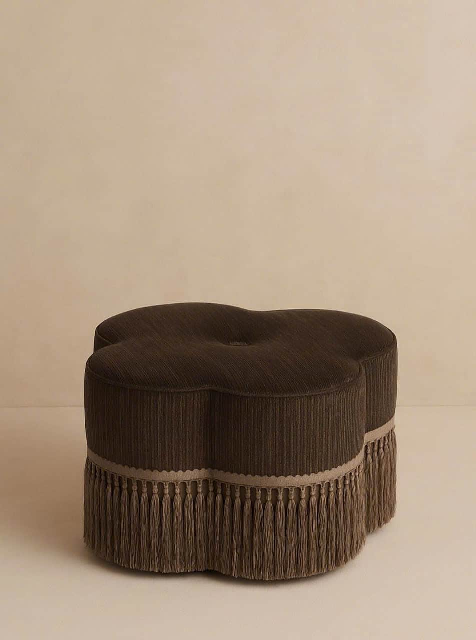 A dark brown, clover-shaped ottoman featuring ribbed upholstery fabric and a decorative fringe trim… — 3D model