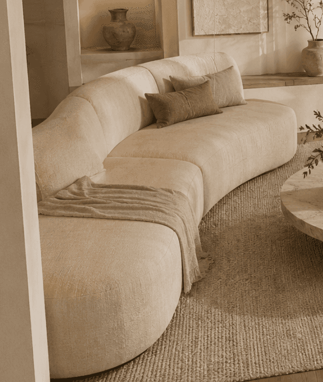 A large, modern, curved sectional sofa upholstered in a light beige, textured fabric. It features a… — 3D model