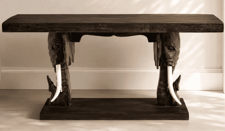 A dark wooden console table featuring intricately carved elephant heads as supports, complete with w… — 3D model