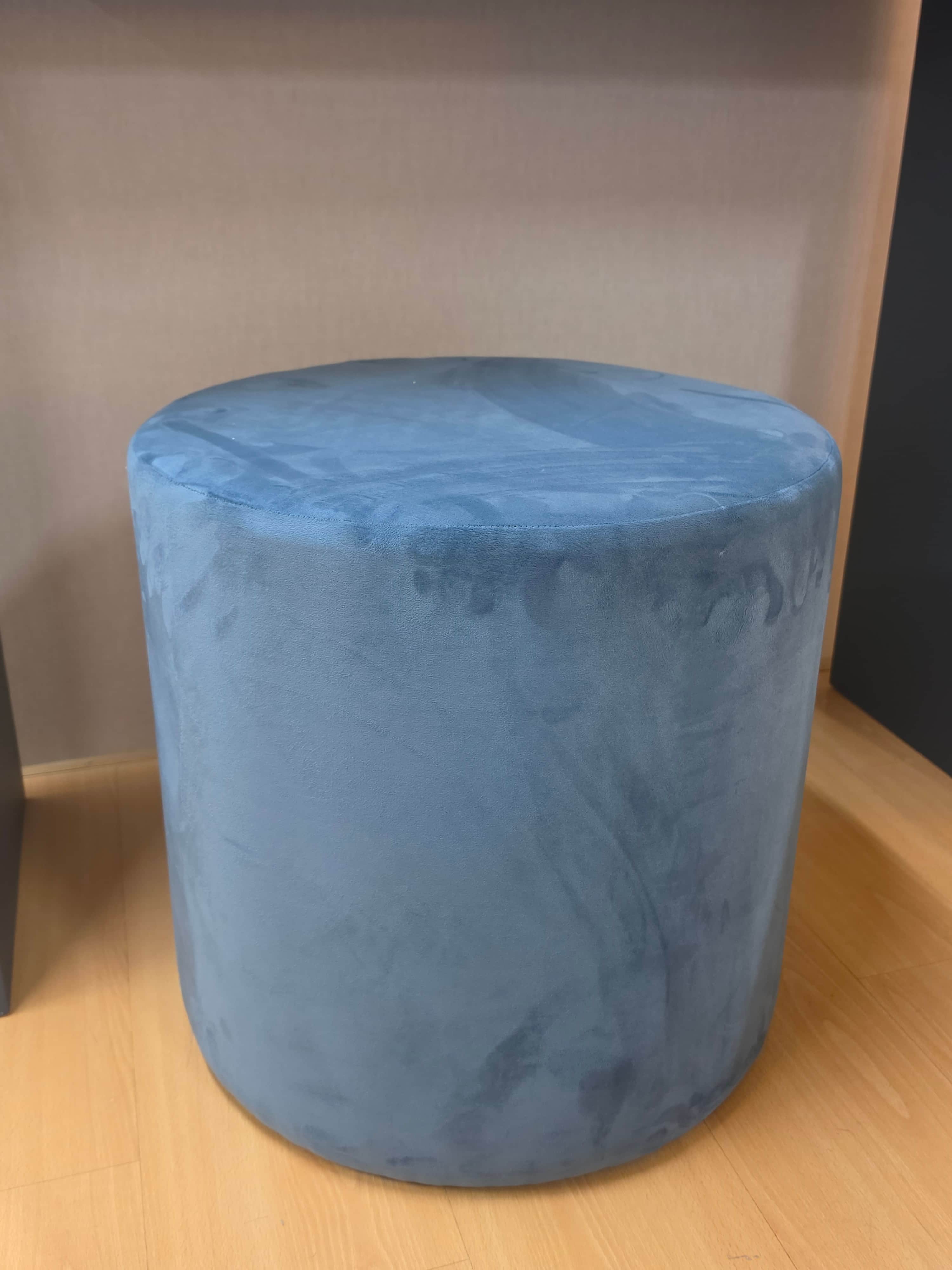 A cylindrical ottoman, fully upholstered in a plush, blue-gray velvet fabric. The ottoman presents a… — 3D model