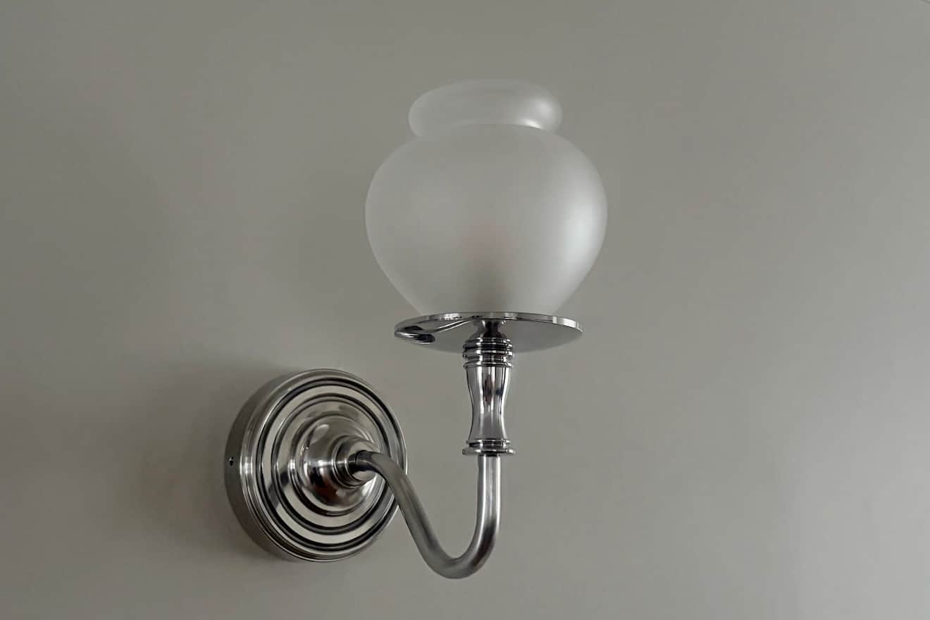 A polished nickel or chrome wall sconce featuring a frosted glass shade in an urn-like shape. The ar… — 3D model