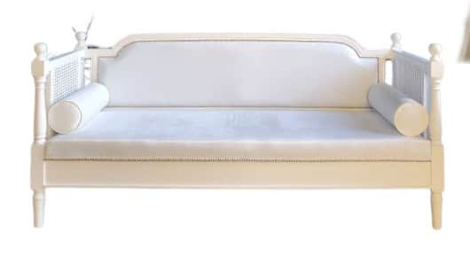 A white daybed featuring a solid wood frame, cane webbing details on the arms, and an upholstered ba… — 3D model