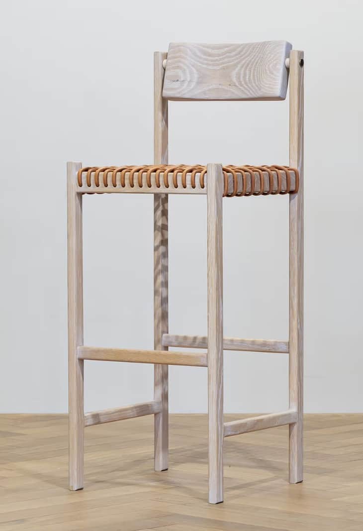 A tall bar stool with a light wood frame and a woven seat and backrest. The frame consists of four v… — 3D model