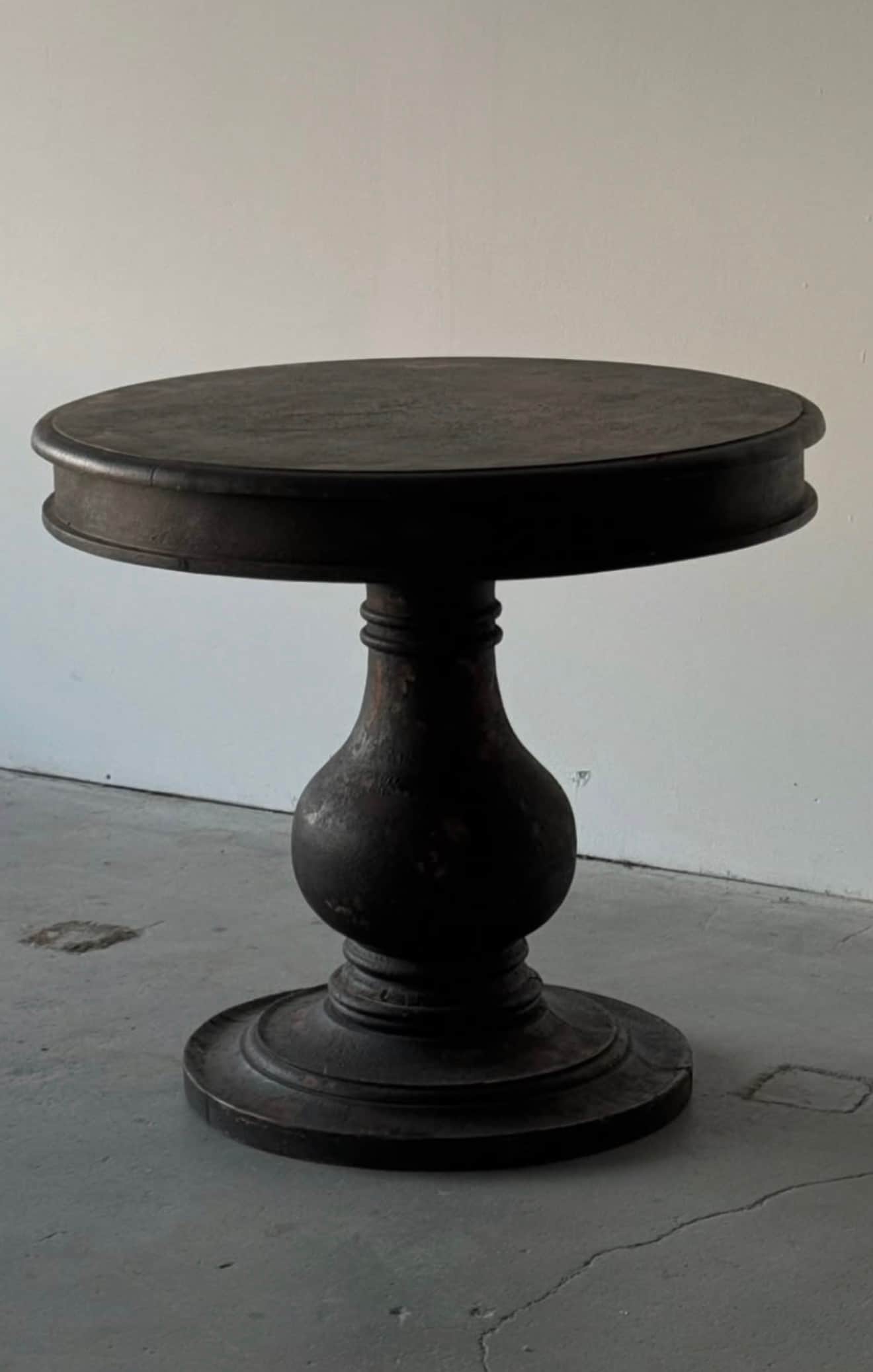 A small, round accent table featuring a dark, distressed finish and a single turned pedestal base. T… — 3D model
