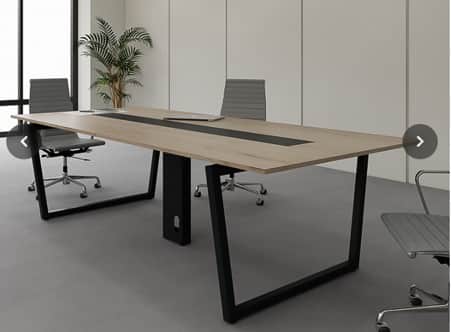 A long, rectangular conference table featuring a light wood-grain laminate top with a prominent blac… — 3D model