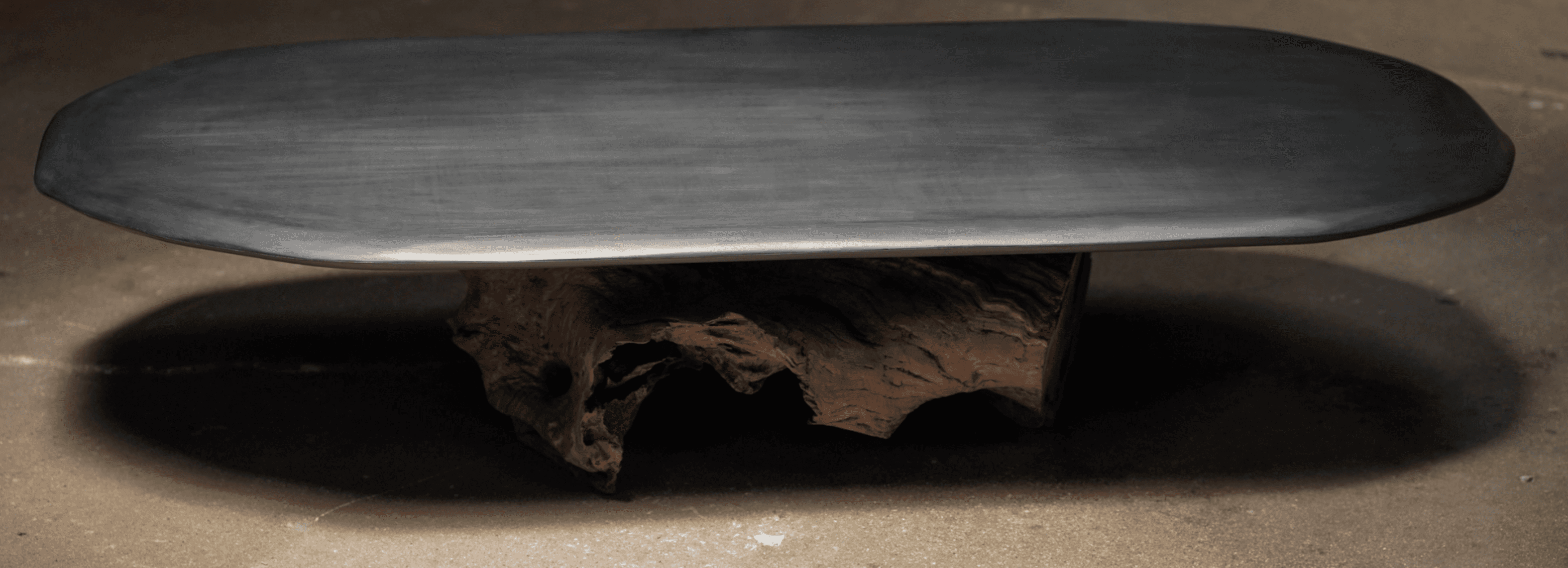 A low coffee table featuring an elongated oval top made of dark, matte material, possibly stone, sup… — 3D model