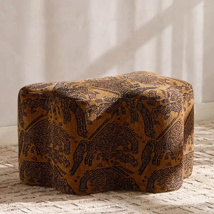 A plush, organically shaped ottoman, upholstered in a brown fabric with a dark, intricate tribal or… — 3D model