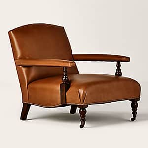 A traditional armchair upholstered in rich brown leather, featuring turned wooden front legs and arm… — 3D model