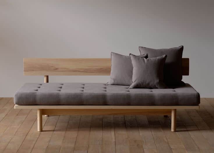 A modern daybed featuring a light-toned wooden frame and a grey upholstered cushion. The frame inclu… — 3D model