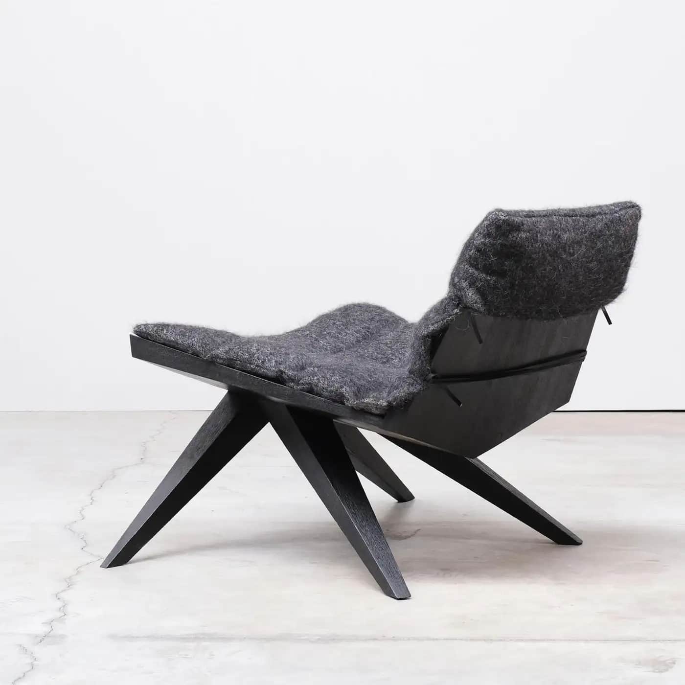 A low-profile, modern lounge chair featuring a dark, angular wooden frame and a thick, soft grey fel… — 3D model