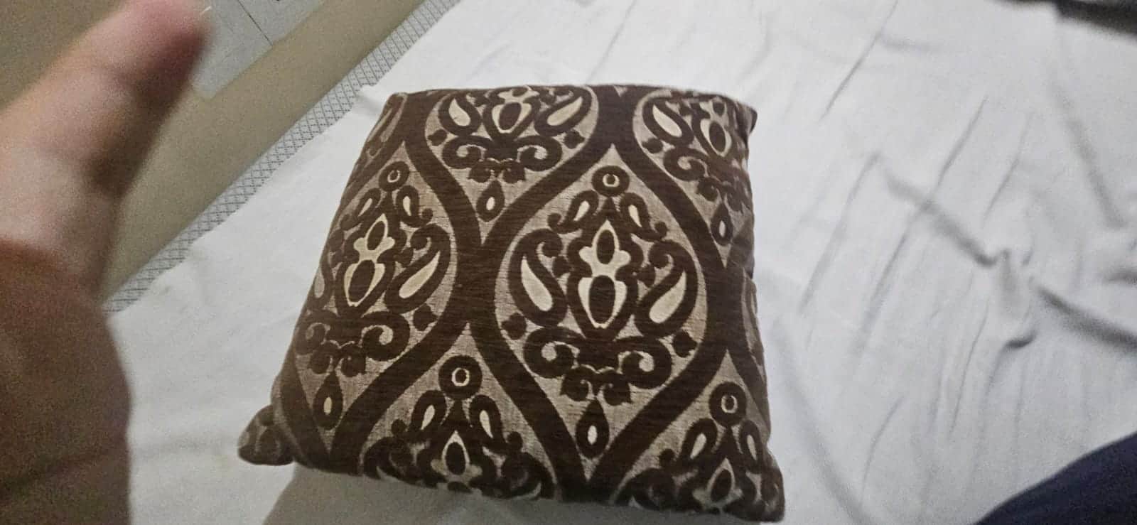 A decorative cushion with a damask-like pattern in dark brown and beige. It appears to be resting on… — 3D model