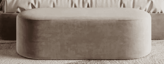 A low-profile, elongated oval ottoman with full upholstery in a neutral beige or taupe color. Its se… — 3D model
