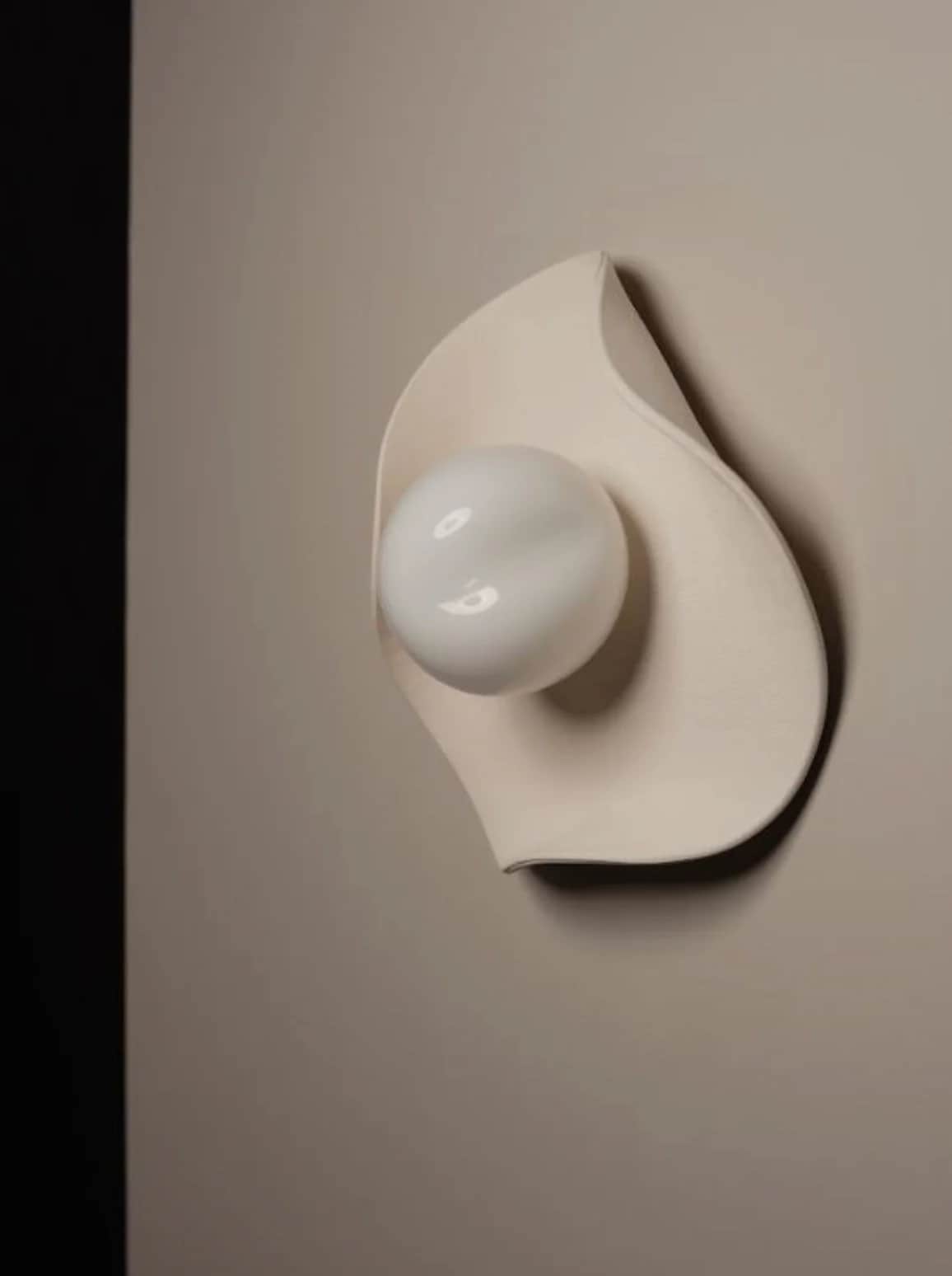 A modern sculptural wall sconce featuring an organic, leaf-like cream-colored backplate made of cera… — 3D model