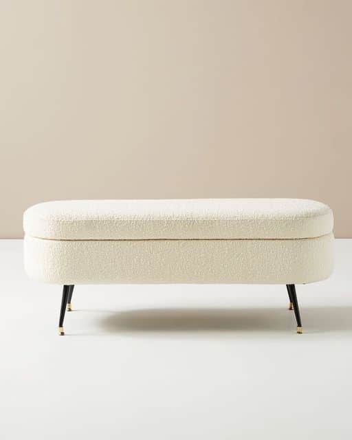 An oval-shaped, off-white boucle upholstered storage bench with slender black metal legs featuring b… — 3D model