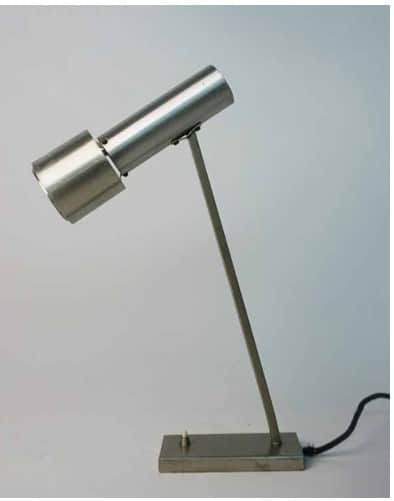 A minimalist silver-colored desk lamp featuring a rectangular base, a slender angled arm, and a cyli… — 3D model
