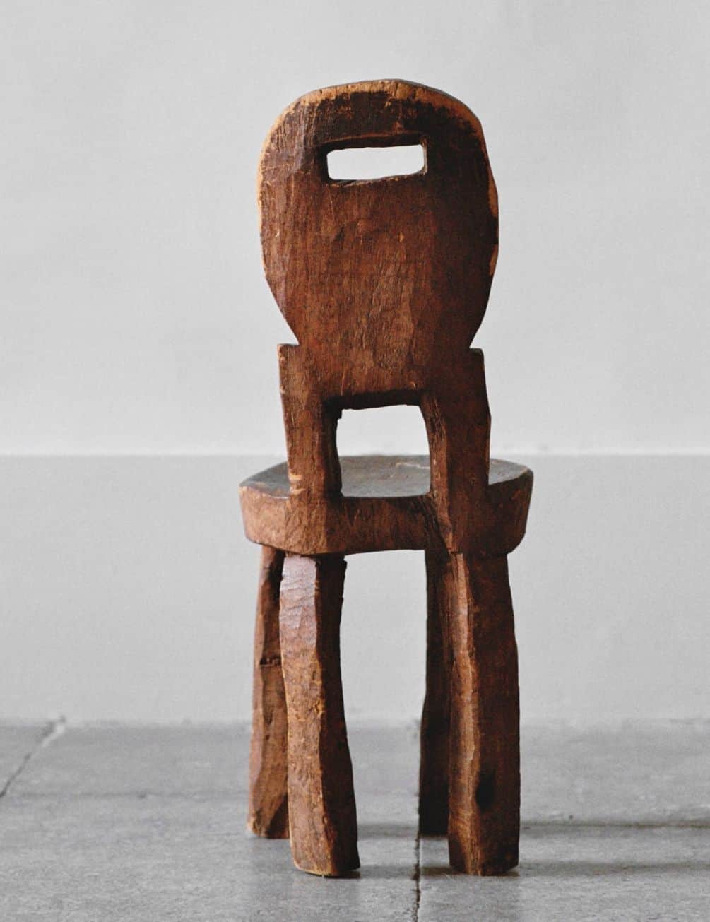 A small, rustic wooden chair featuring a round seat, four splayed legs, and a carved backrest with a… — 3D model