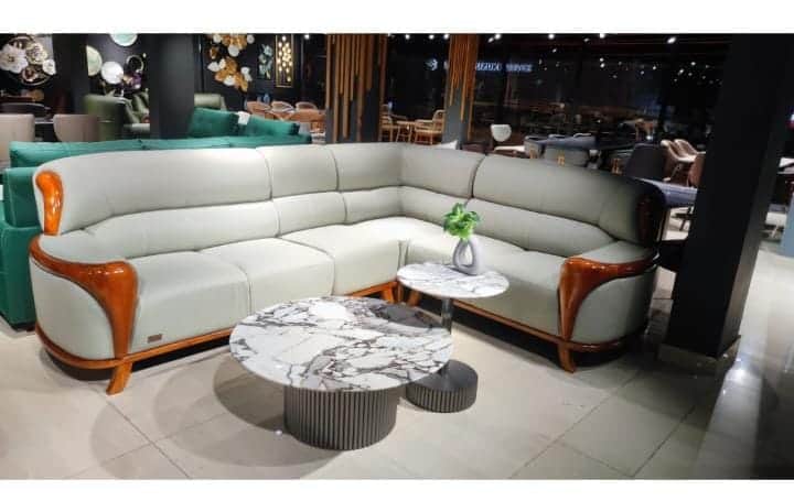 An L-shaped sectional sofa upholstered in light grey material, possibly leather, featuring prominent… — 3D model