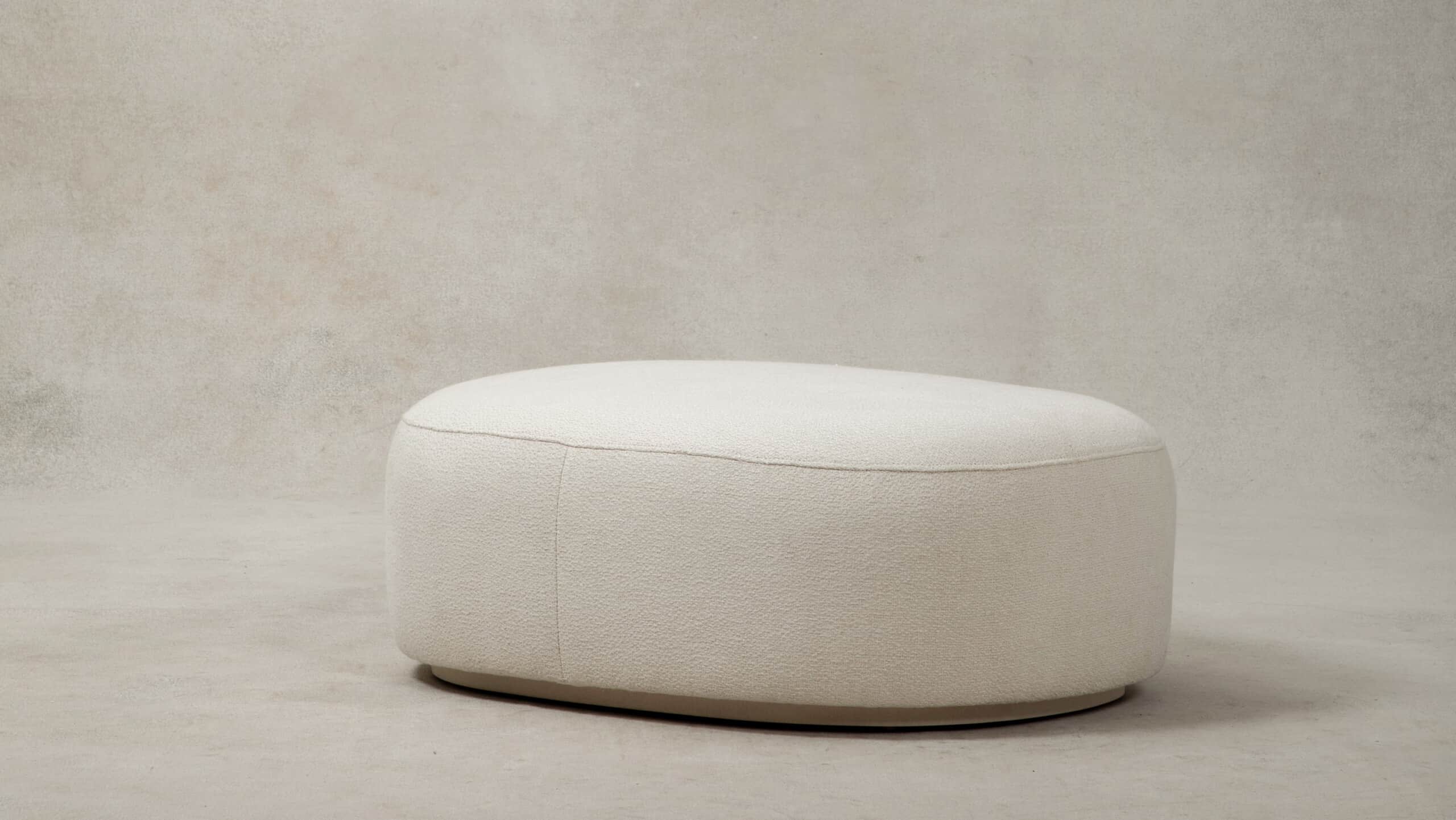 A contemporary upholstered ottoman with a rounded oval shape, covered in a plush cream bouclé fabric… — 3D model