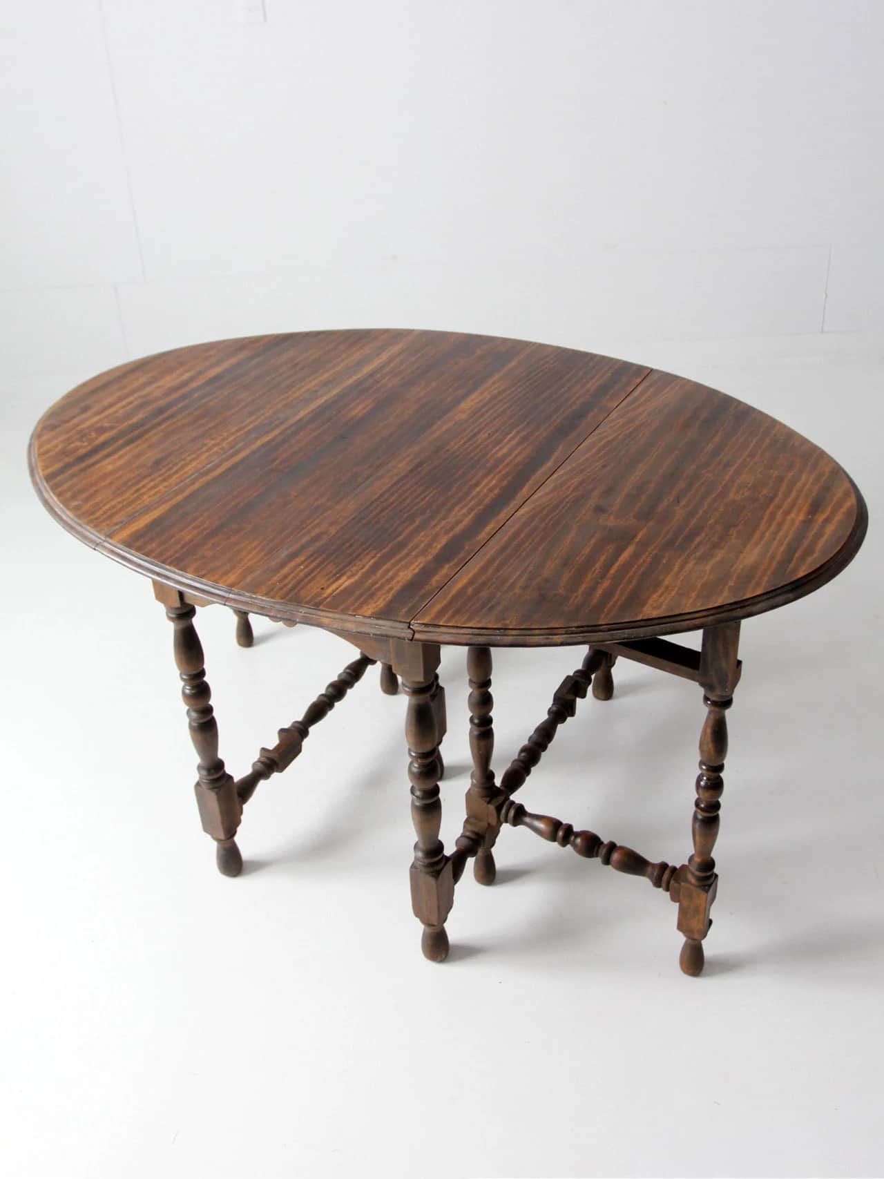 A traditional dark-stained wood drop-leaf gateleg table with an oval top. The base features turned b… — 3D model