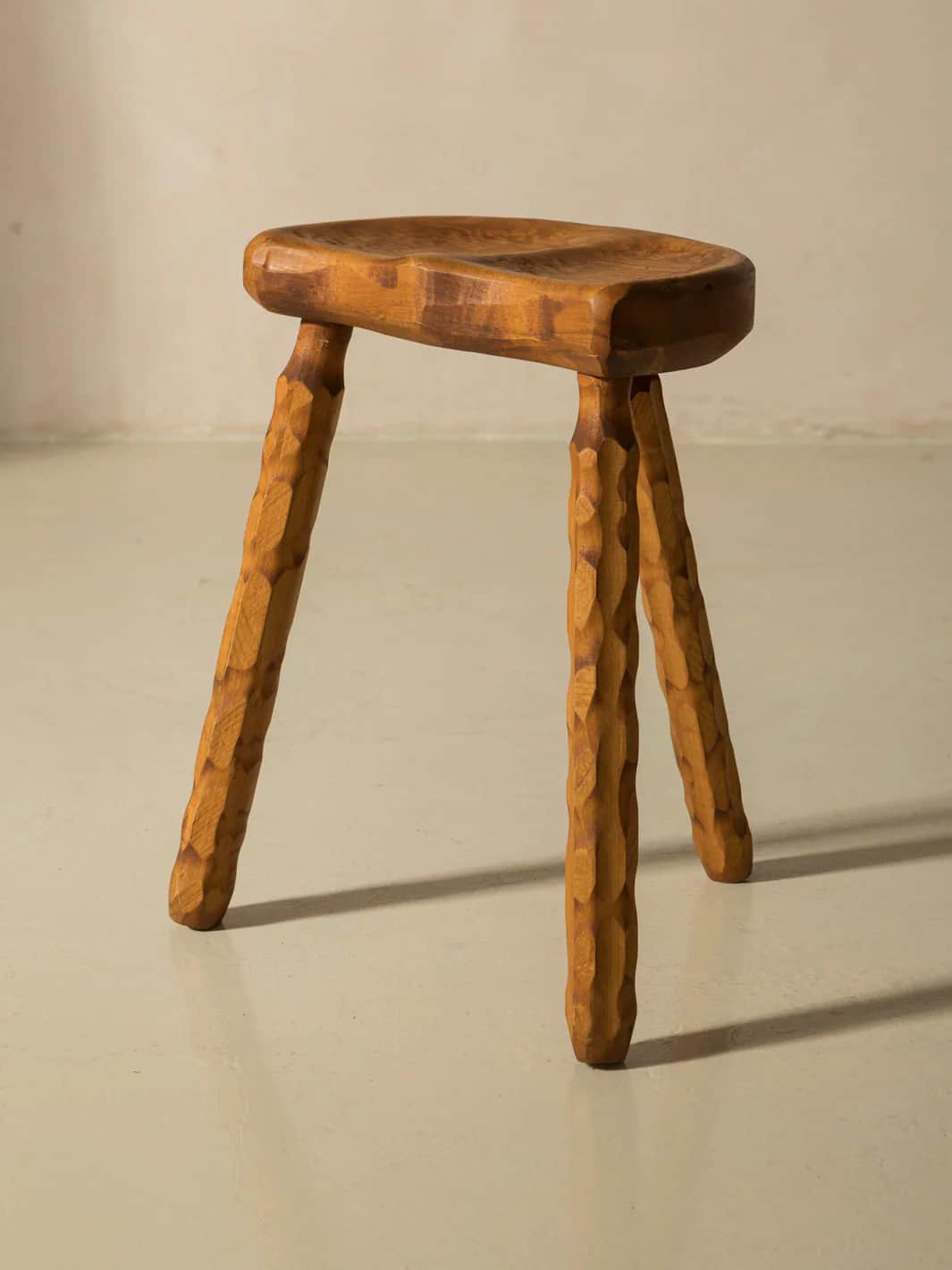 A three-legged wooden stool with an oval, contoured seat. The legs are carved with a textured patter… — 3D model