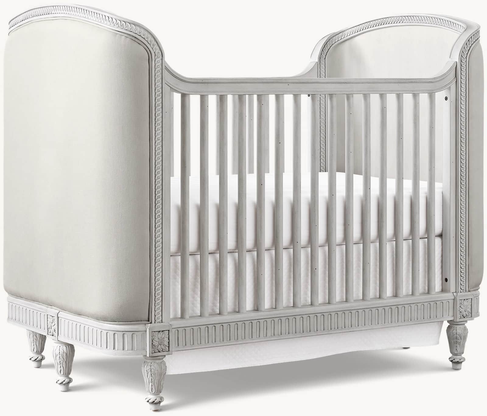A classic-style crib with upholstered side panels and a slatted front and back. The frame is painted… — 3D model