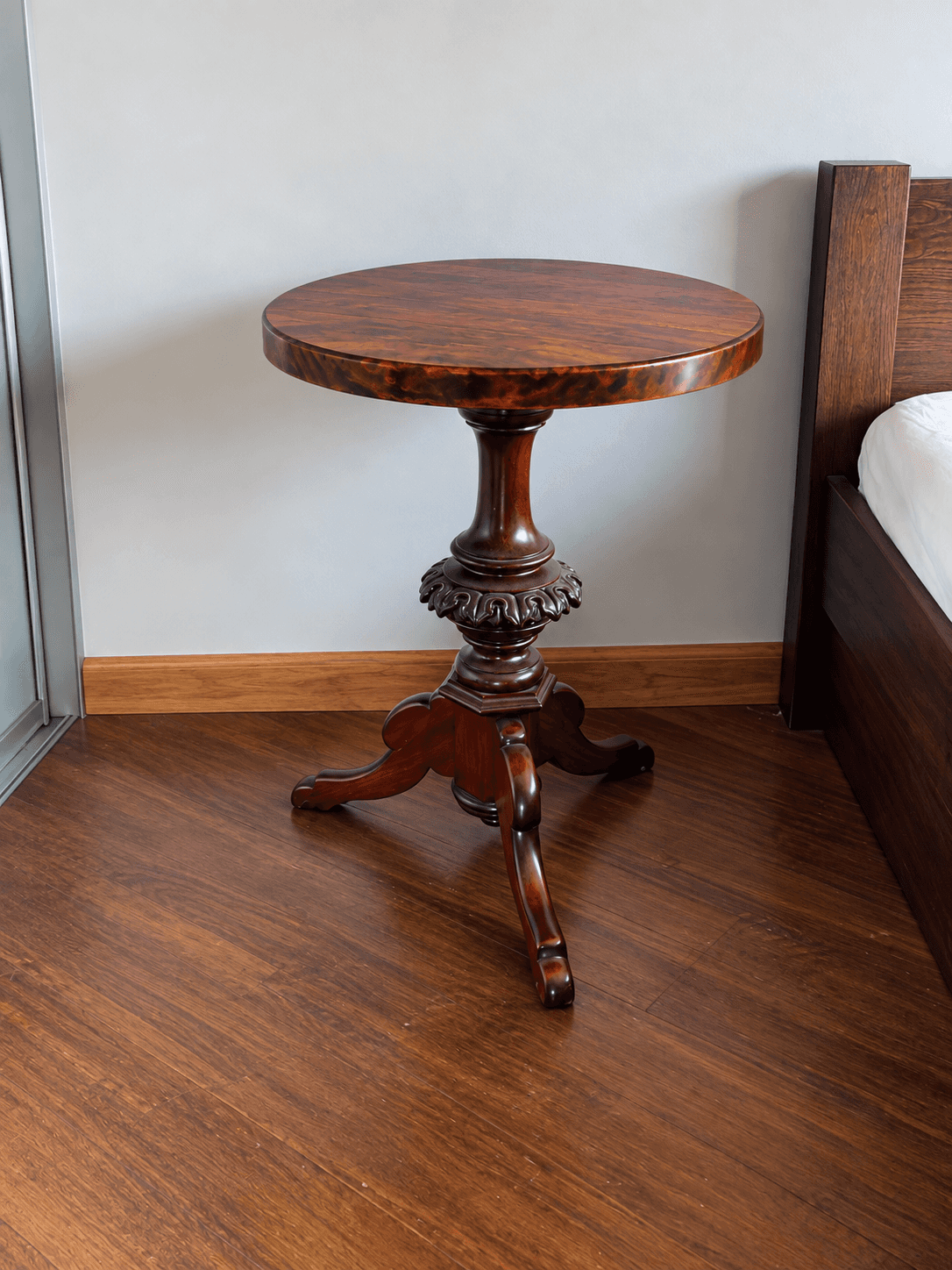A round, dark wood pedestal table featuring a polished tabletop with visible wood grain, a turned an… — 3D model
