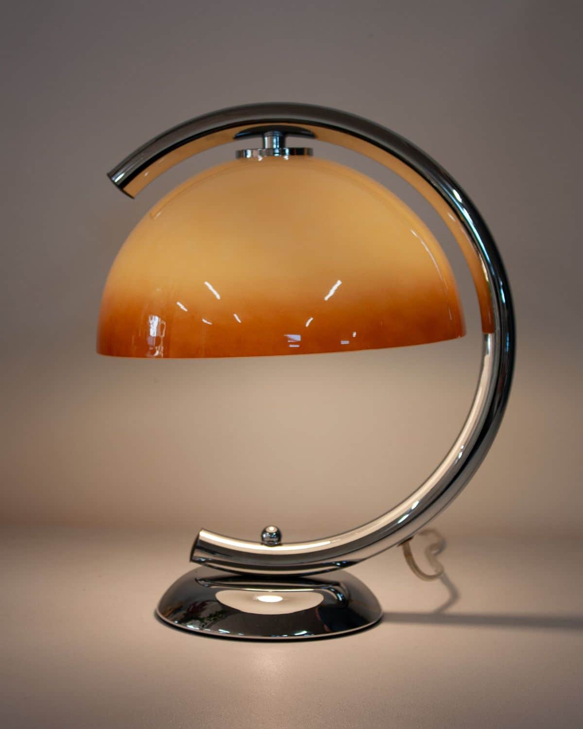 A contemporary table lamp featuring a polished chrome arc frame supporting a frosted amber glass dom… — 3D model
