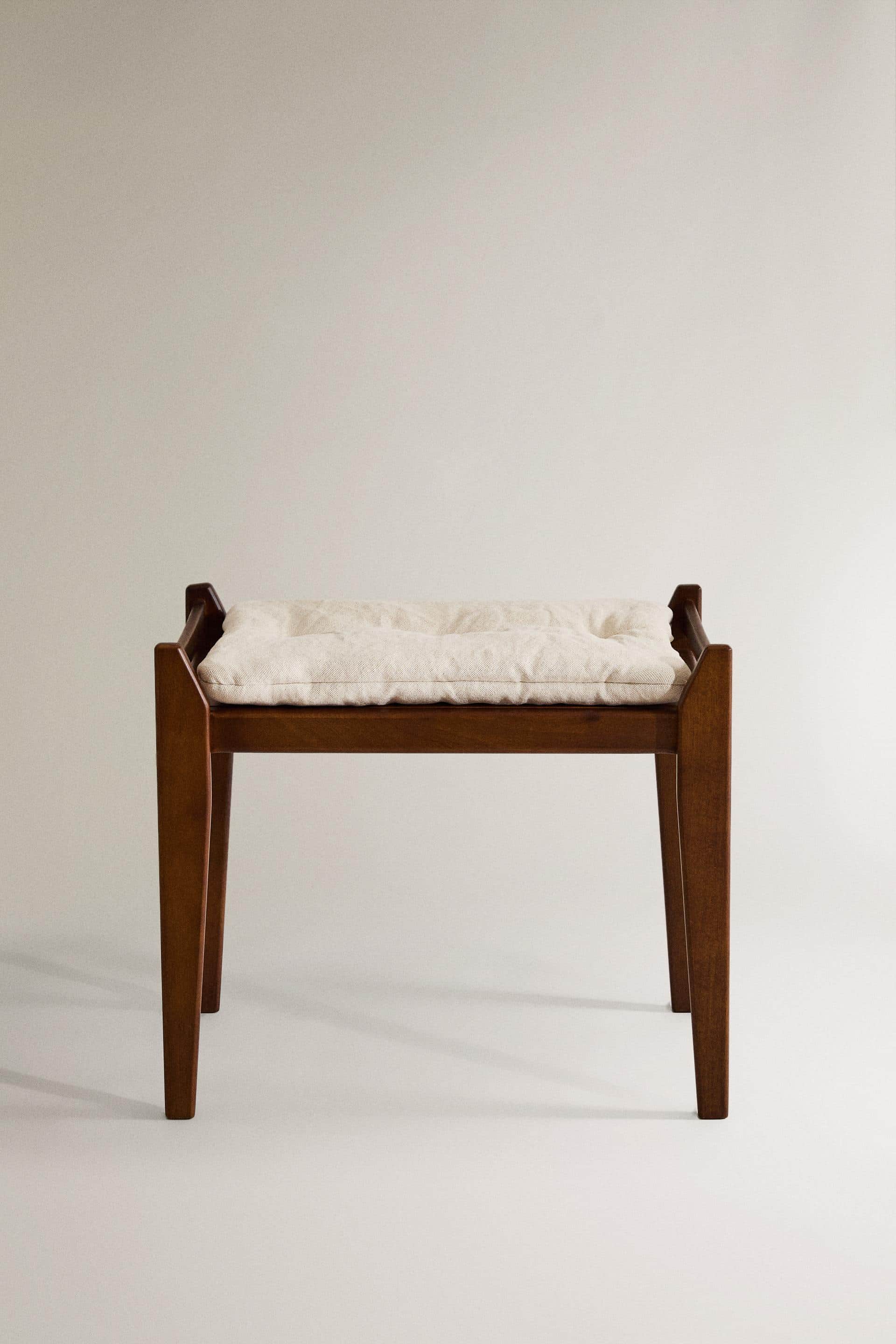 A wooden ottoman with a tufted, upholstered seat. The frame is constructed from dark wood with a vis… — 3D model
